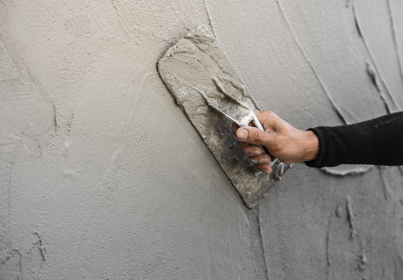 Hand plasterer plastering gray cement wall background, hand worker brush rough concrete wall for smooth manual well free space for text with occupations about building construction