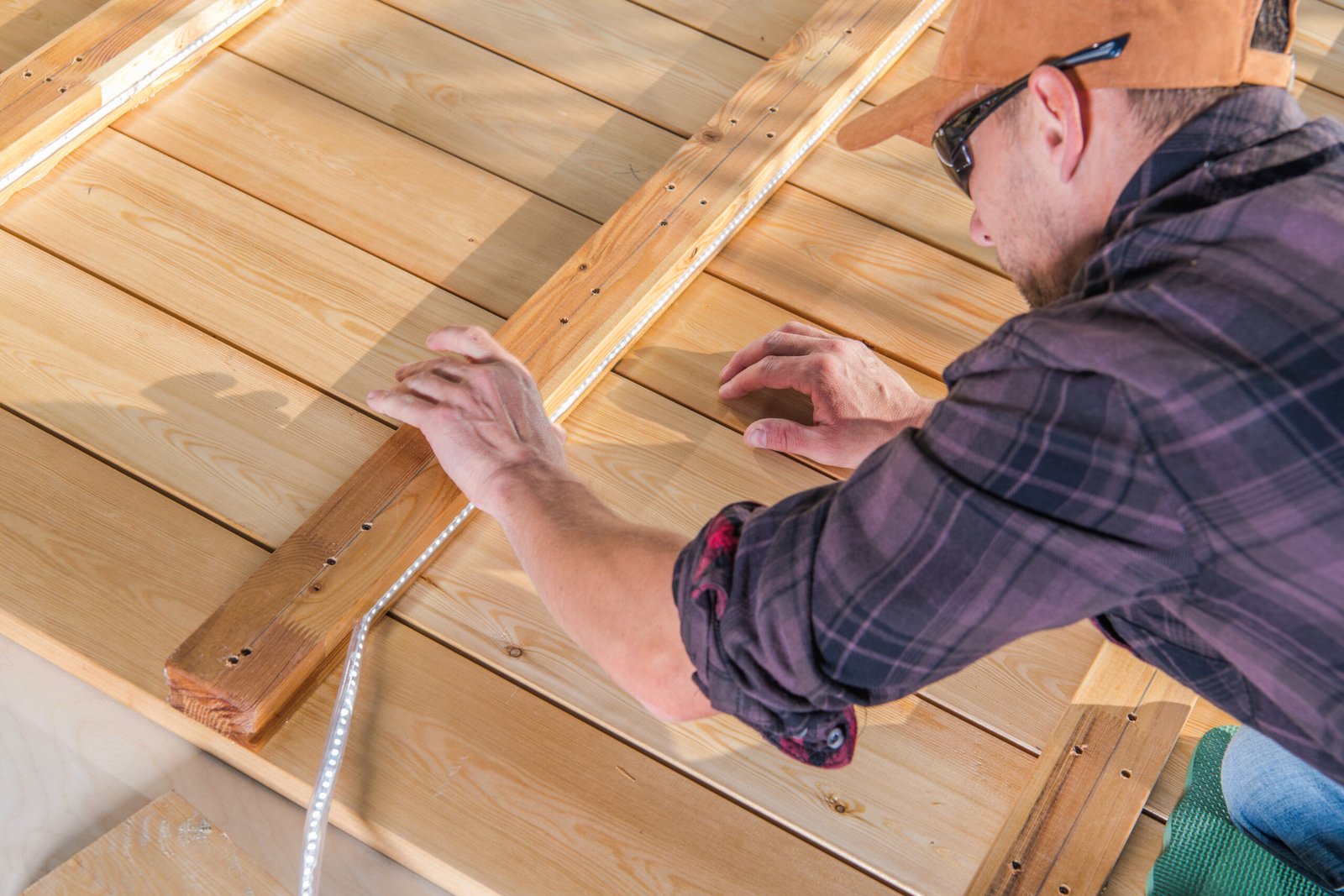 Worker Installing LED Light Tape Inside Wooden Elements of Newly Built Deck. Woodwork Theme.