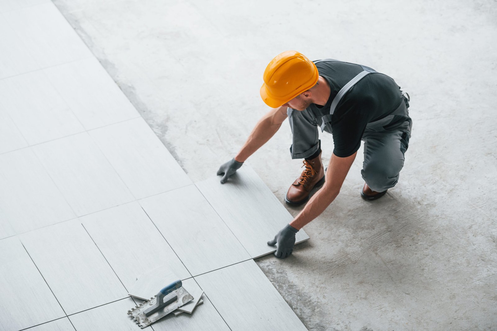 Installation of plate. Man in grey uniform and orange hard hat works indoors in modern big office at daytime.
