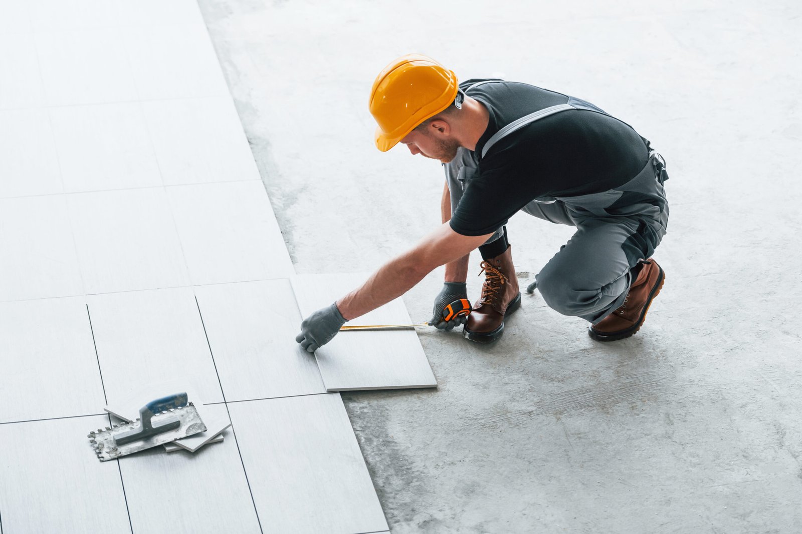 Installation of plate. Man in grey uniform and orange hard hat works indoors in modern big office at daytime.
