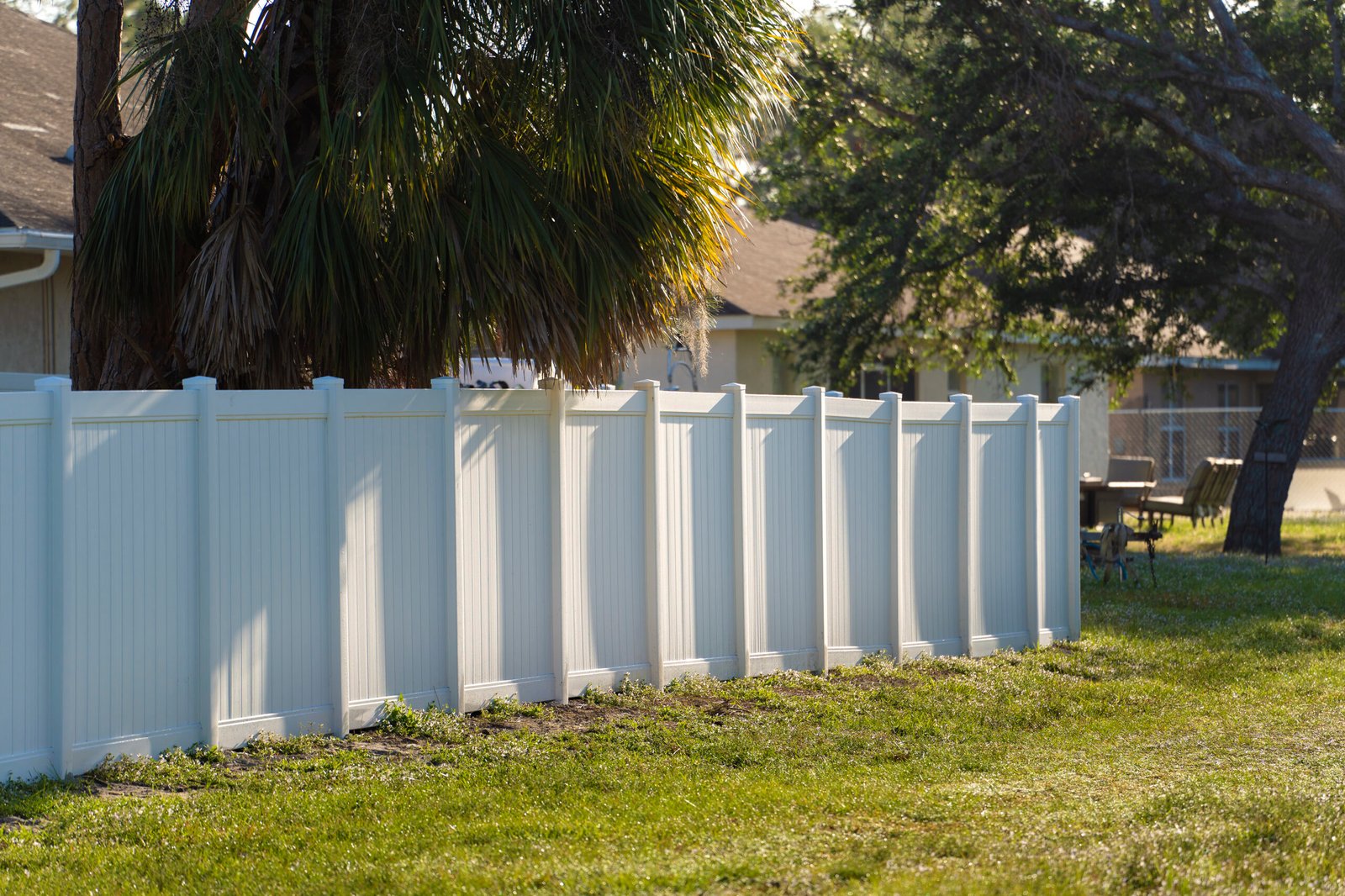 White vinyl picket fence on green lawn surrounding property grounds for backyard protection and privacy.