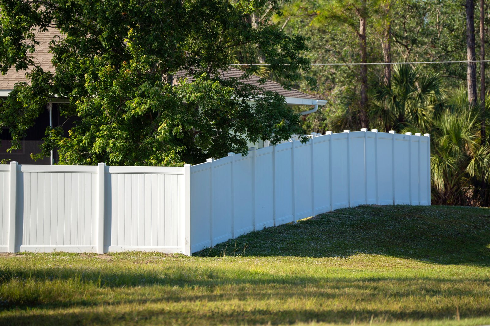 White vinyl picket fence on green lawn surrounding property grounds for backyard protection and privacy.