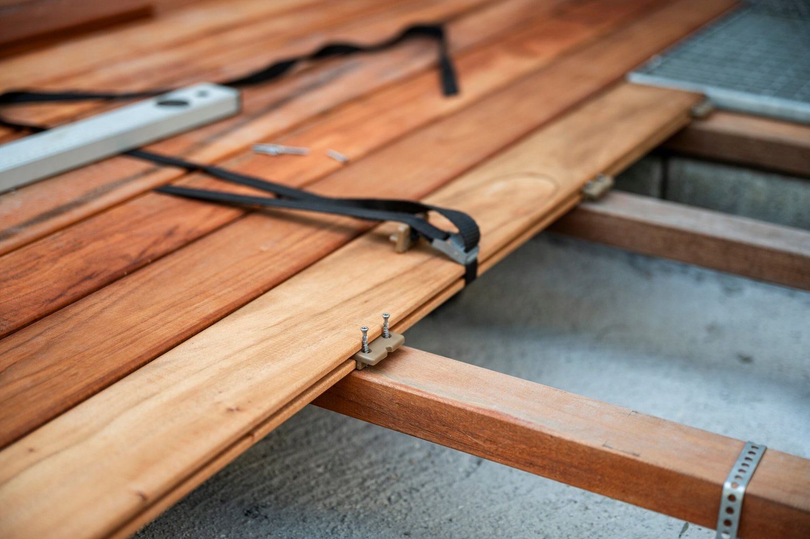 A close-up of wooden decking being installed with hidden fasteners and tools. Wooden planks are securely attached to joists with screws, straps, and brackets.
